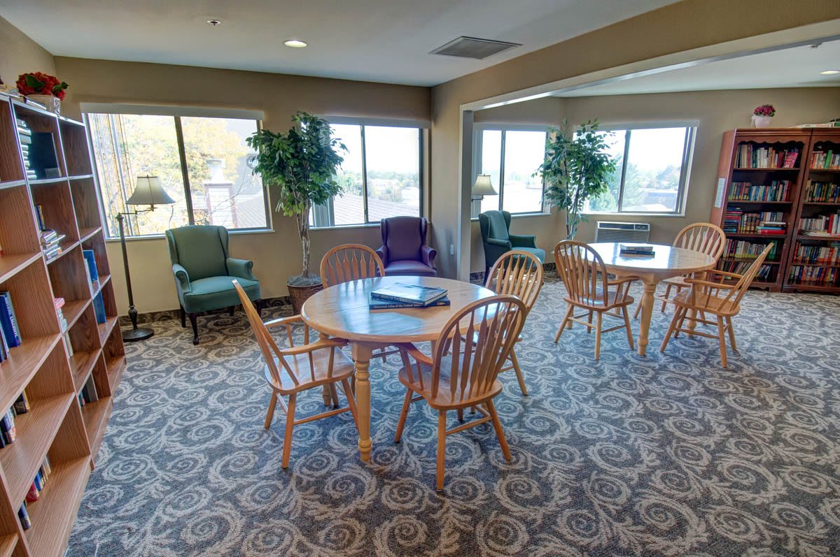A cozy lounge area with tables, chairs, and large windows letting in natural light.