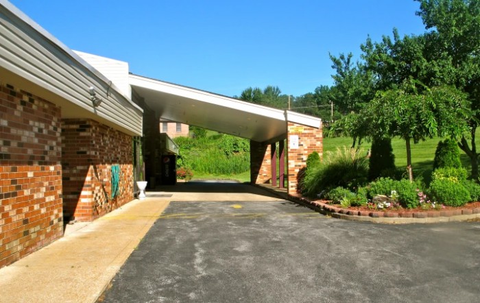 A building with a covered driveway surrounded by greenery on a sunny day.