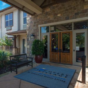 The entrance to a building featuring stone walls, glass doors, and outdoor seating.