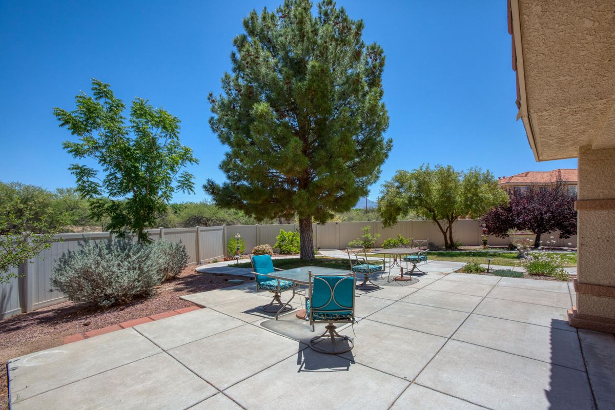 A sunny backyard patio area with outdoor furniture and trees.