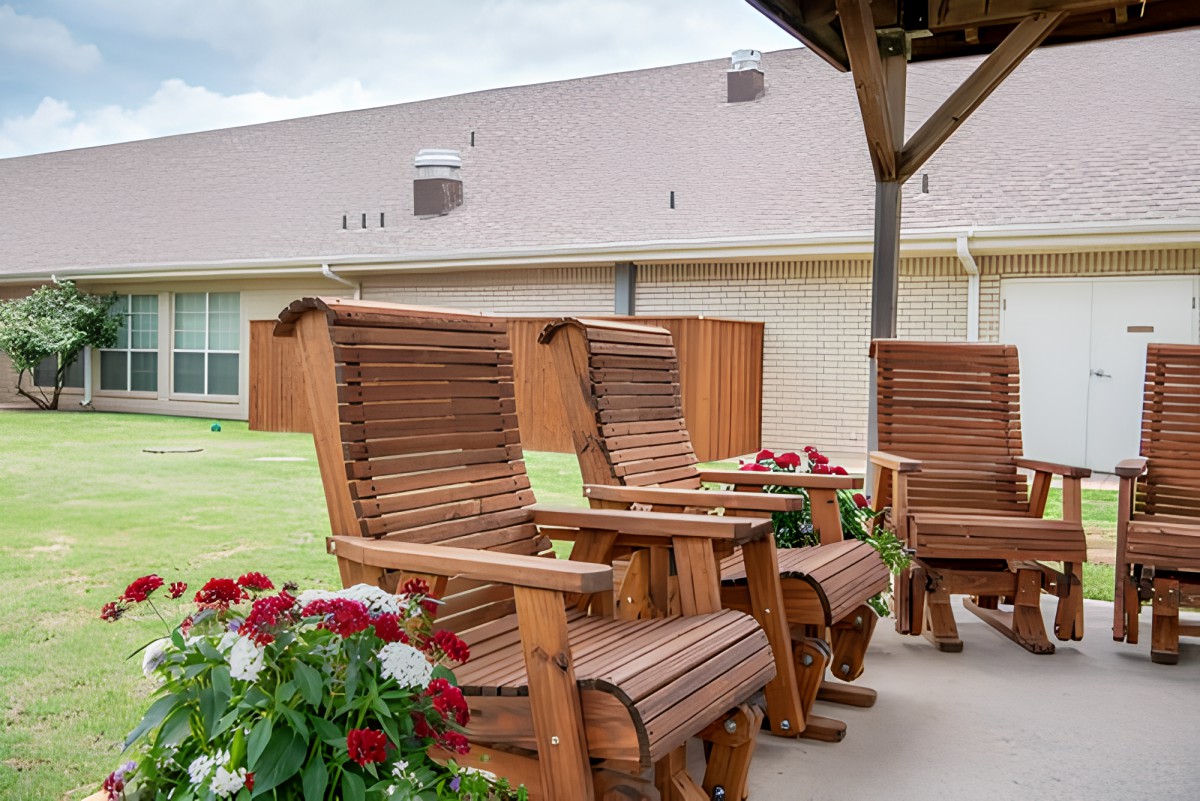 Wooden patio chairs under a shelter with flowers nearby.