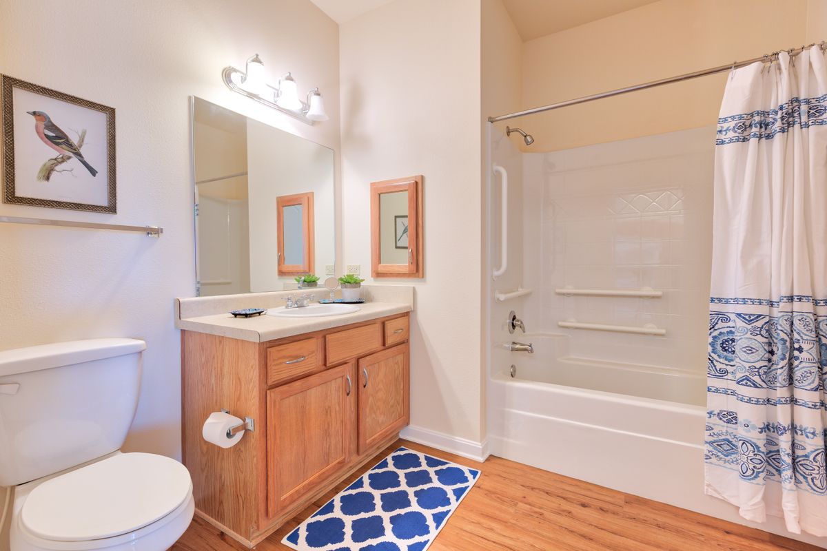 A clean and well-lit bathroom with a wooden cabinet, mirror, bathtub, and decorative elements.