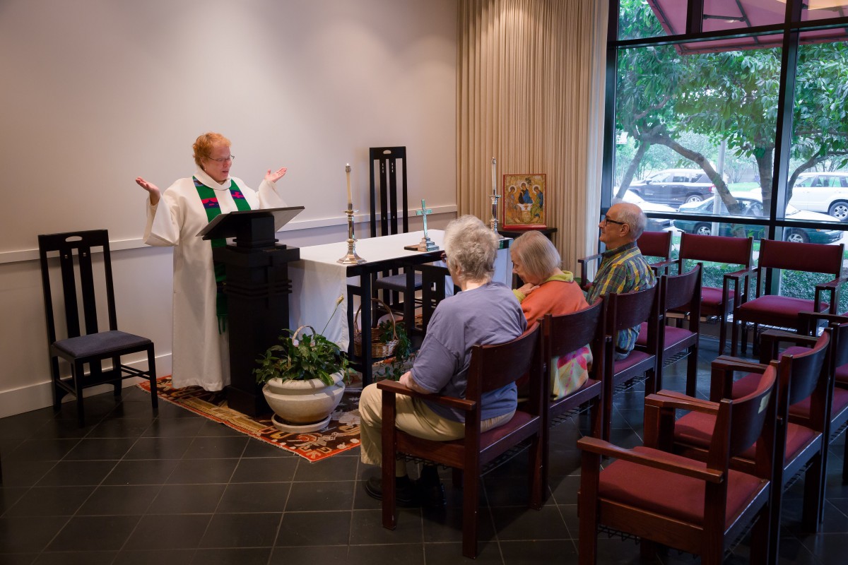 A priest conducting a service in a small chapel with a few attendees.