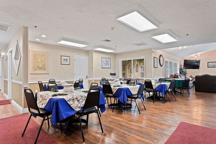 A spacious dining area with tables and chairs neatly arranged, featuring blue tablecloths on a hardwood floor.