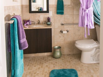 A bathroom featuring colorful towels and a bathrobe, with a sink, mirror, and toilet.