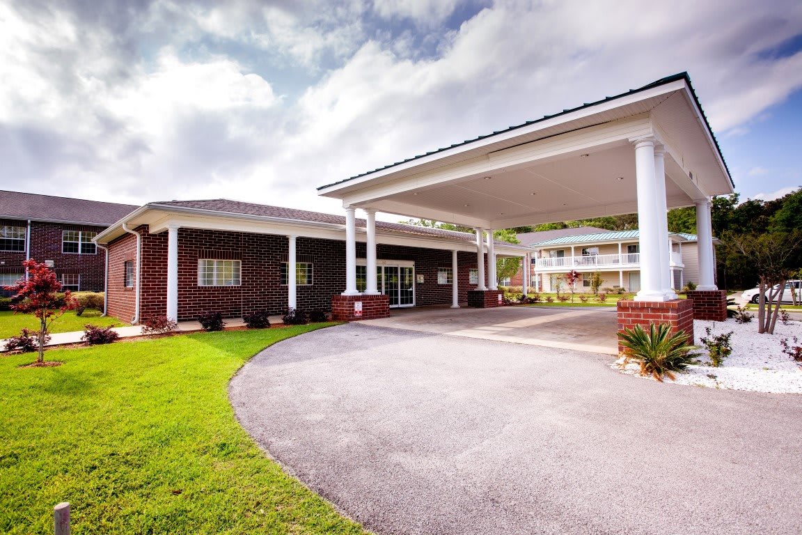 A well-maintained building entrance with white columns and a circular driveway under a partly cloudy sky.