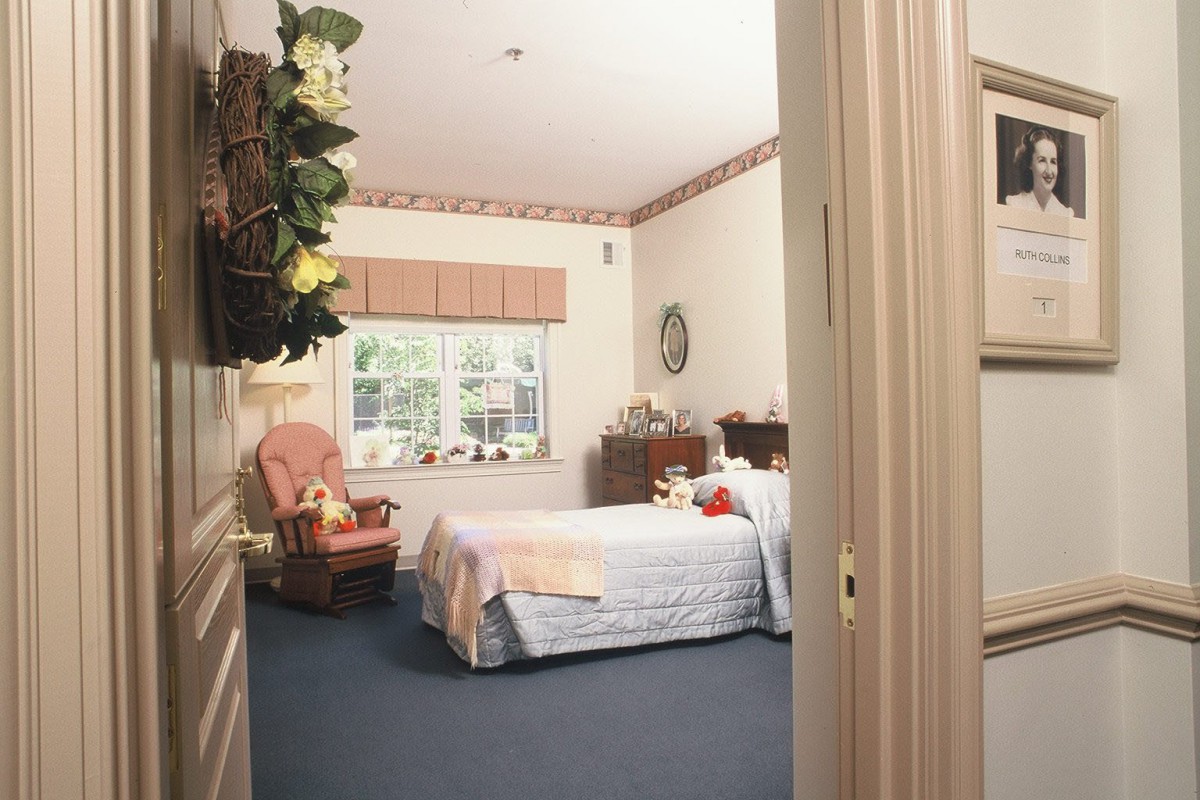 A cozy bedroom with a neatly made bed, armchair, and window offering natural light.