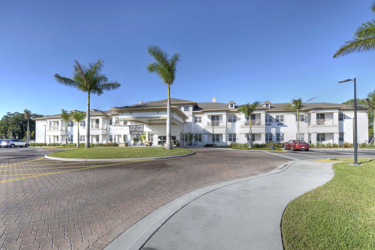 A sunny view of a large white building surrounded by palm trees and a paved road.