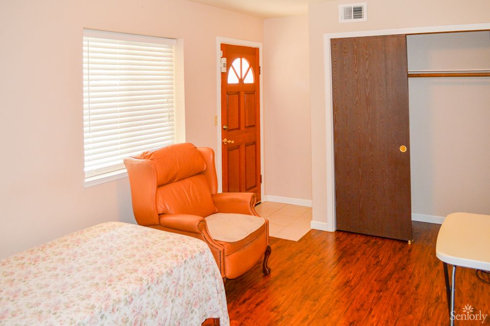 A cozy bedroom with an armchair, wooden door, and a window.