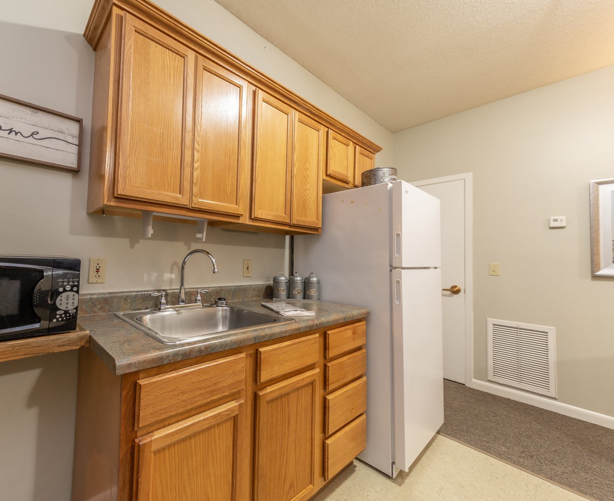 A compact kitchen featuring wooden cabinets, a refrigerator, and a sink.