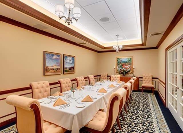 An elegantly set formal dining room with a long table, plush chairs, and artwork on the walls.