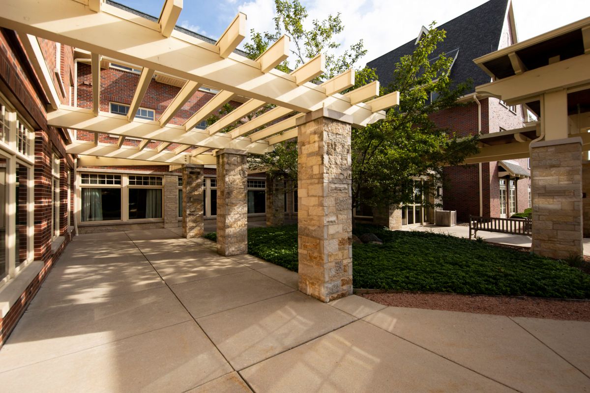 A courtyard featuring a pergola and landscaping with trees.