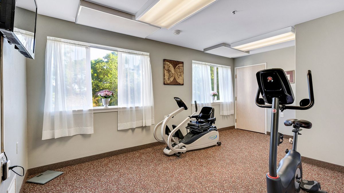 A bright exercise room with a cardio machine and large windows.