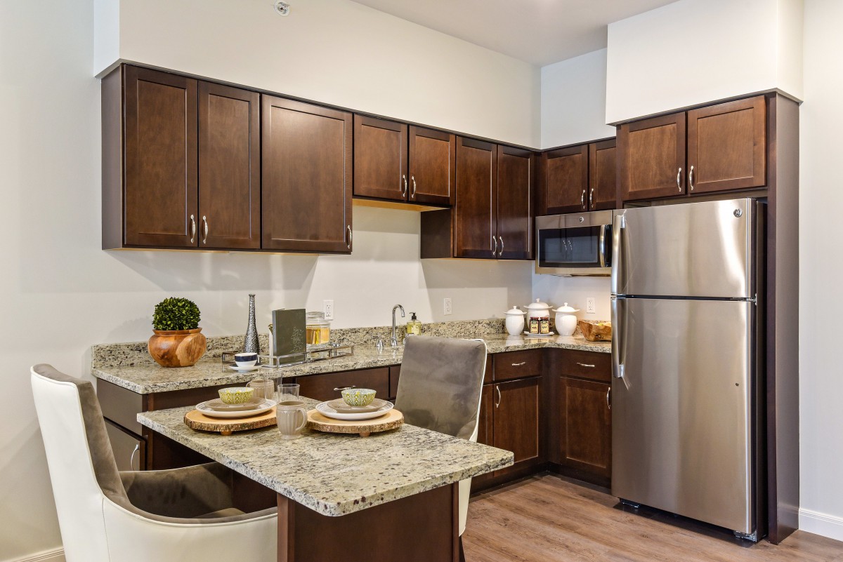 A modern kitchen with wooden cabinets and granite countertops, featuring stainless steel appliances and a small dining area.