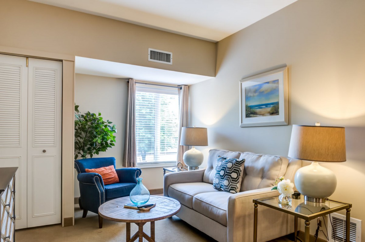 A cozy living room with a sofa, armchair, and coffee table, complemented by decorative lighting and artwork.