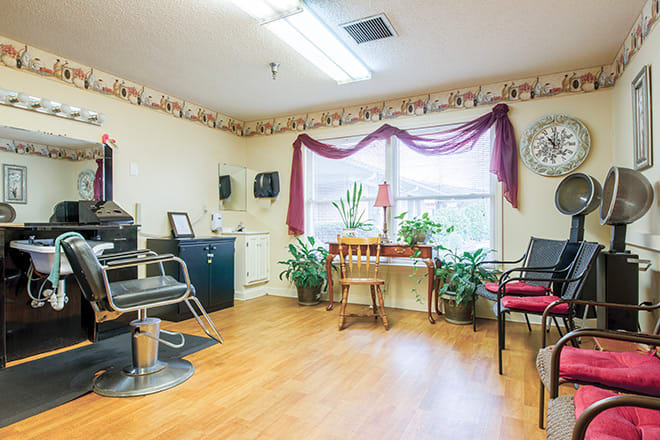 A cozy salon with a waiting area and styling chair, featuring plants by the window.