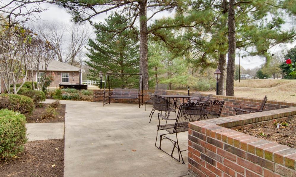 An outdoor patio area with metal furniture surrounded by trees and brick walls.