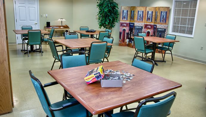 A community center room with tables and chairs set up for activities, featuring a puzzle in progress on one table.