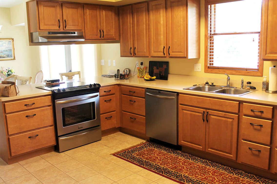 A cozy kitchen with wooden cabinets, stainless steel appliances, and a colorful rug.