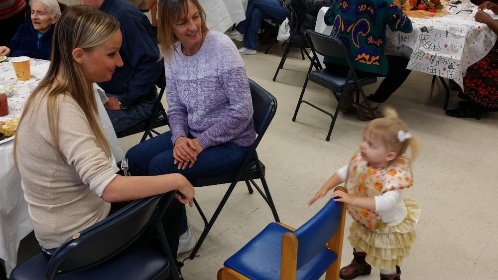 A child and two adults having a conversation indoors while sitting on chairs.