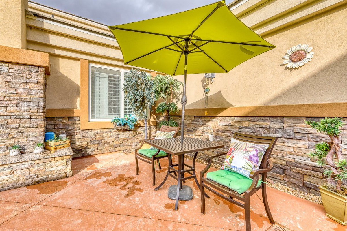 A sunny patio with a green umbrella, two chairs, and a table.