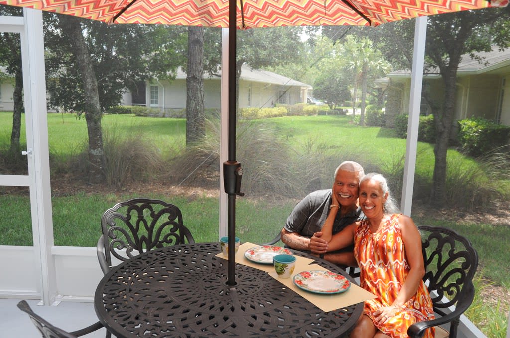 A couple enjoying a meal on their patio under an umbrella.