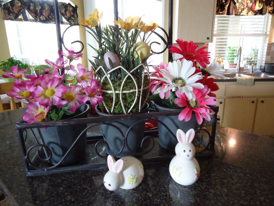 A decorative indoor arrangement featuring colorful flowers and ceramic bunnies, adding a touch of spring cheer.