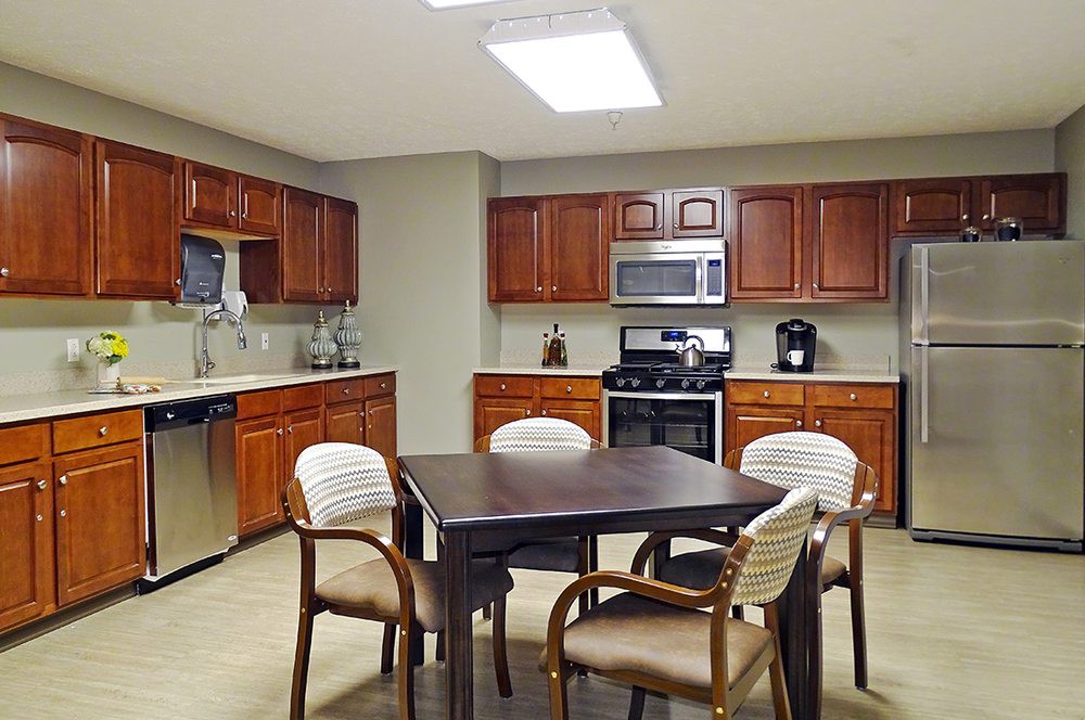 A modern kitchen with wooden cabinets, a central dining table, and stainless steel appliances.