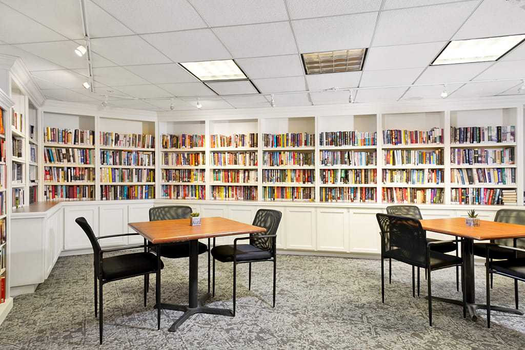 A quiet library reading area with bookshelves lining the walls and several tables with chairs for study.