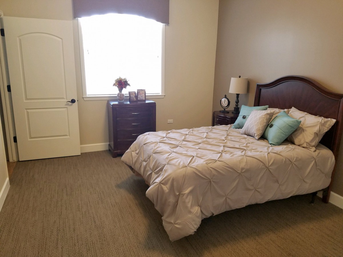 A neatly arranged bedroom with a bed, pillows, dresser, and lamp.