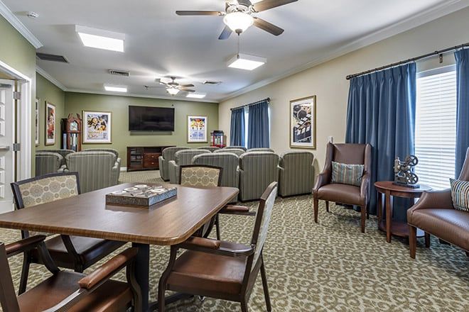 A cozy living room with comfortable seating, a television, tables, and chairs, decorated with artwork on the walls.