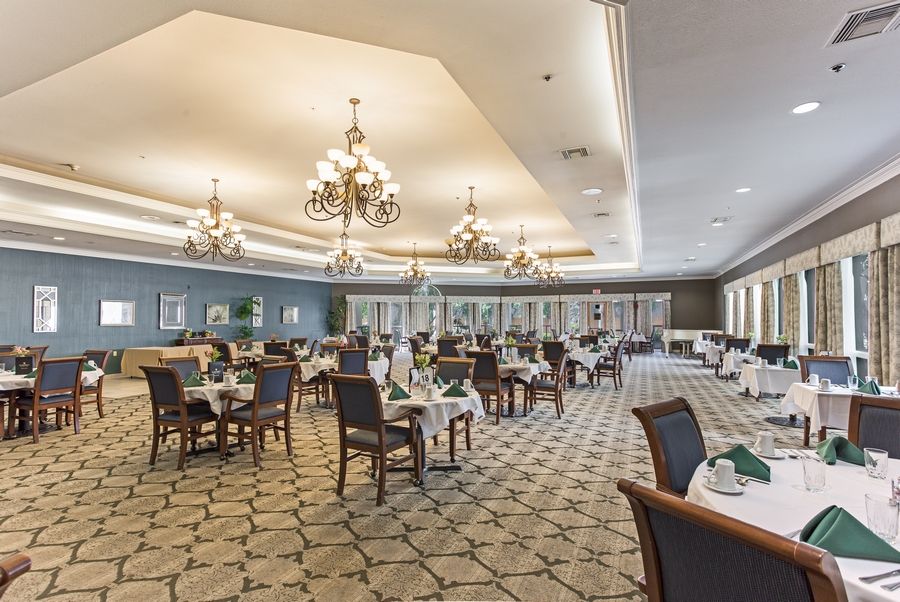 An elegant dining room with chandeliers, set tables, and carpeted flooring.