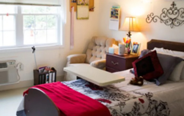 A cozy bedroom with a bed, side table, lamp, and an armchair by the window.