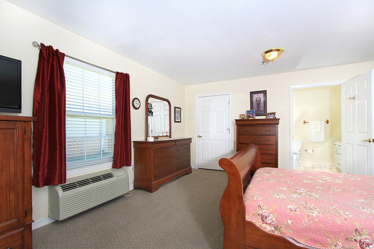 A cozy bedroom with wooden furniture, including a dresser and a mirror, features a window with red curtains.