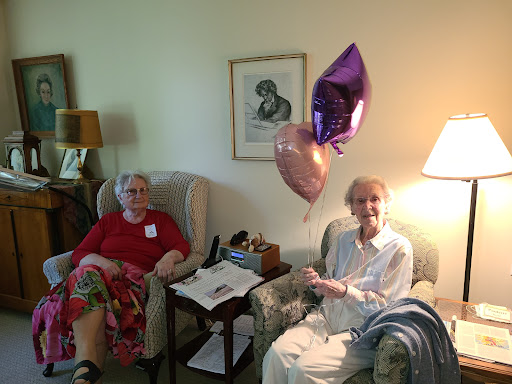 Two elderly women enjoying a moment together with balloons in a cozy indoor setting.