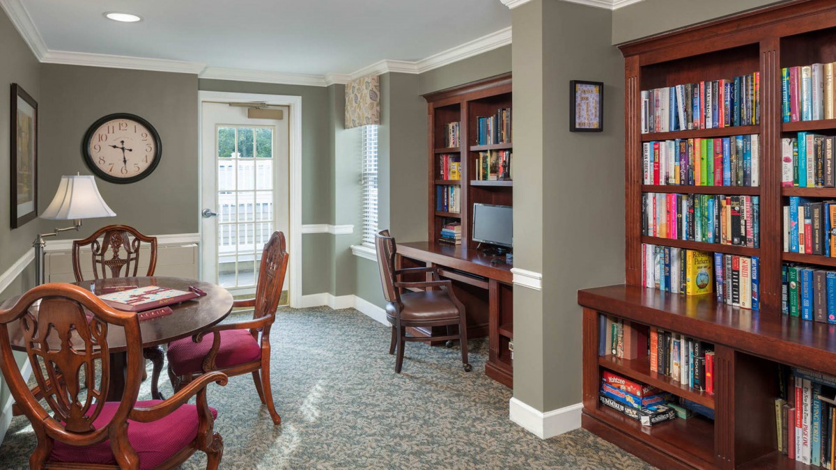 A cozy library interior with bookshelves, a desk, and seating area by the window.
