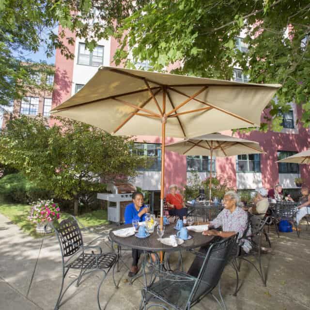 People sitting at an outdoor patio under large umbrellas near a building.