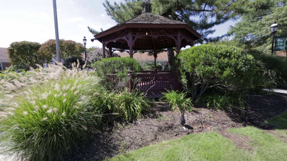 A wooden gazebo surrounded by lush greenery in a garden setting.