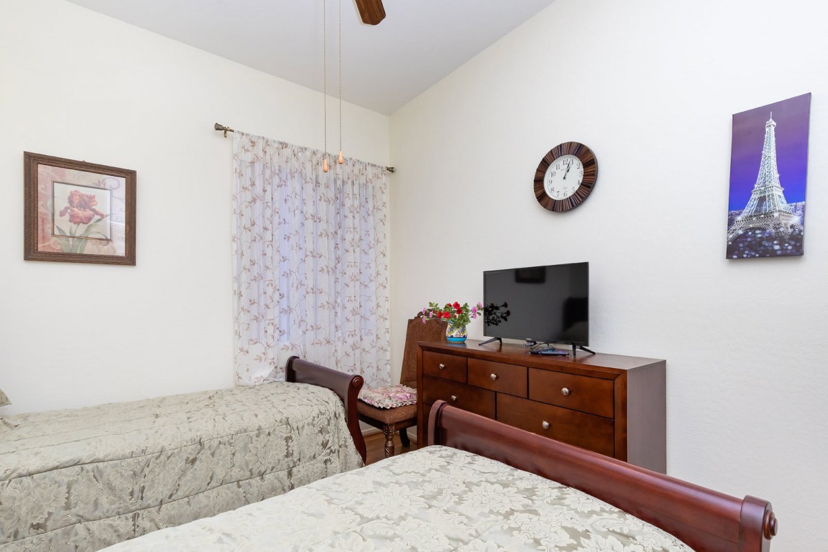 A cozy bedroom with two beds, a TV on a dresser, and a wall clock.