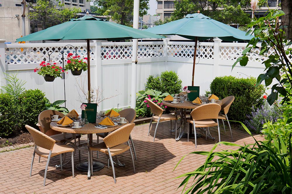 Charming outdoor patio with tables, chairs, and green umbrellas surrounded by lush greenery.