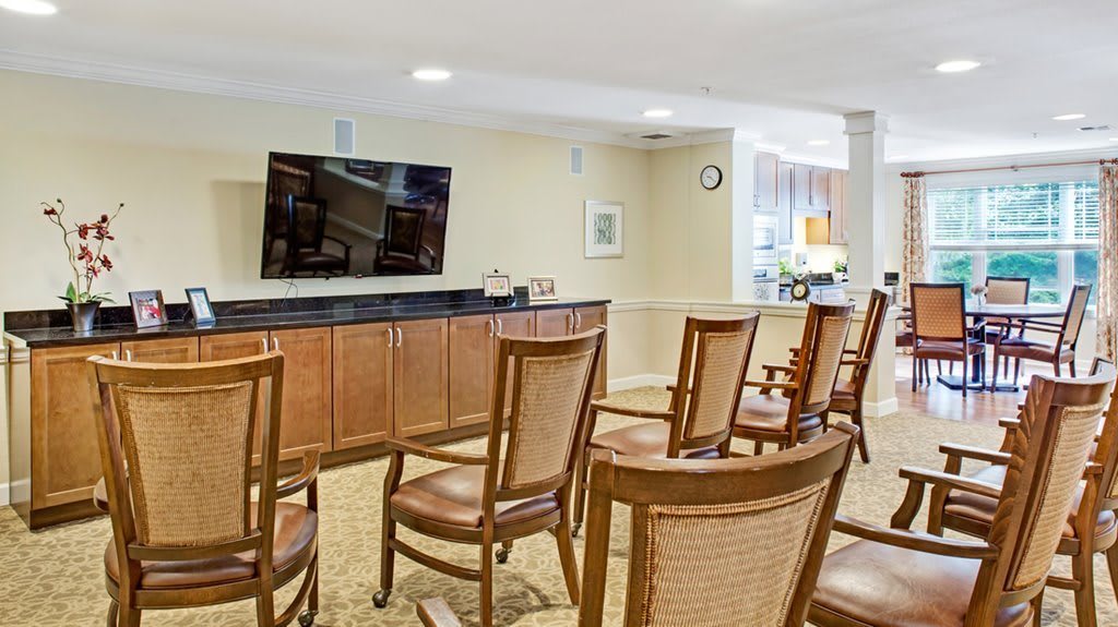 An empty conference room with wooden chairs arranged in rows facing a large television.