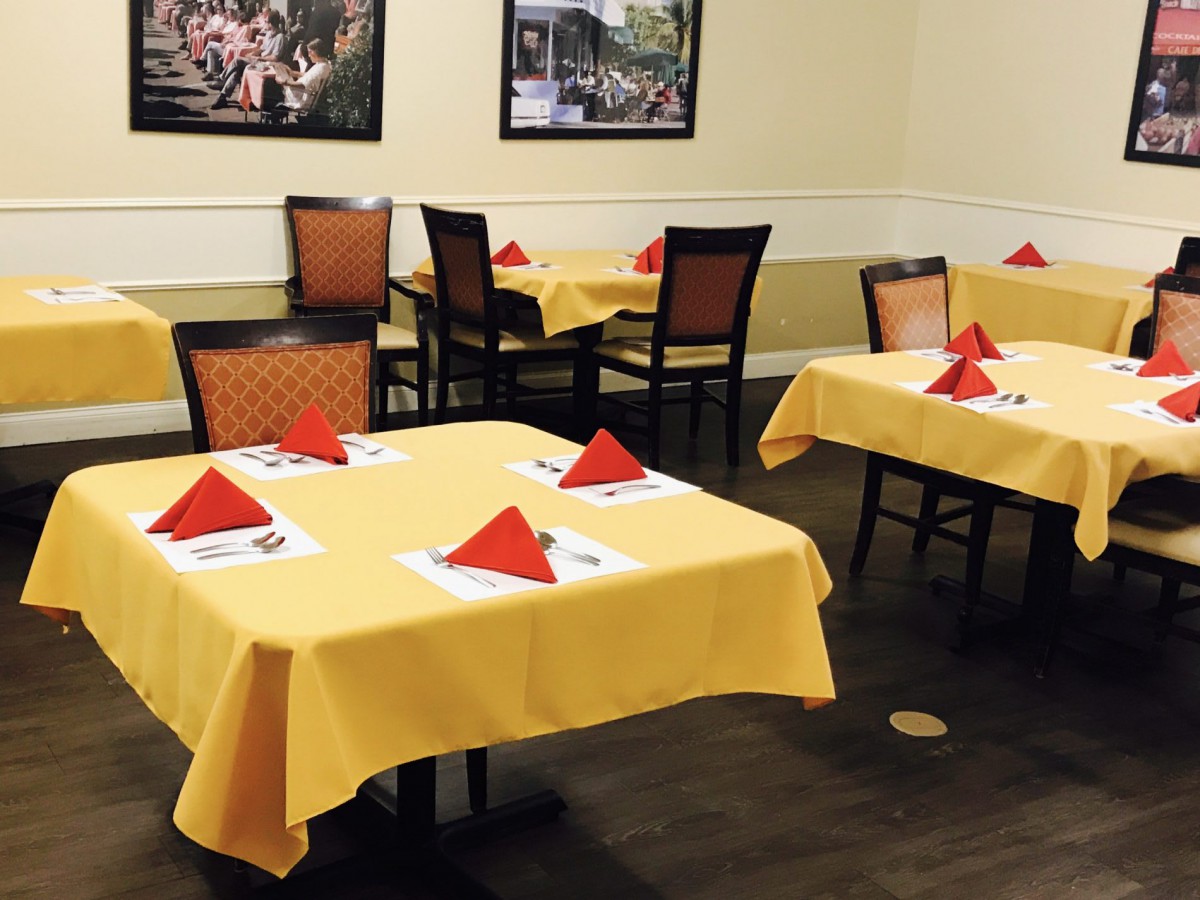 A neatly arranged restaurant dining area featuring tables with yellow tablecloths and red napkins.