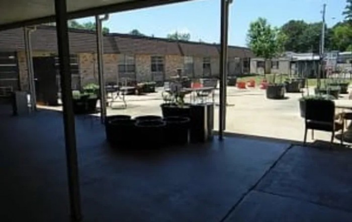 A sunny courtyard with seating areas and tables, partially shaded by a structure.