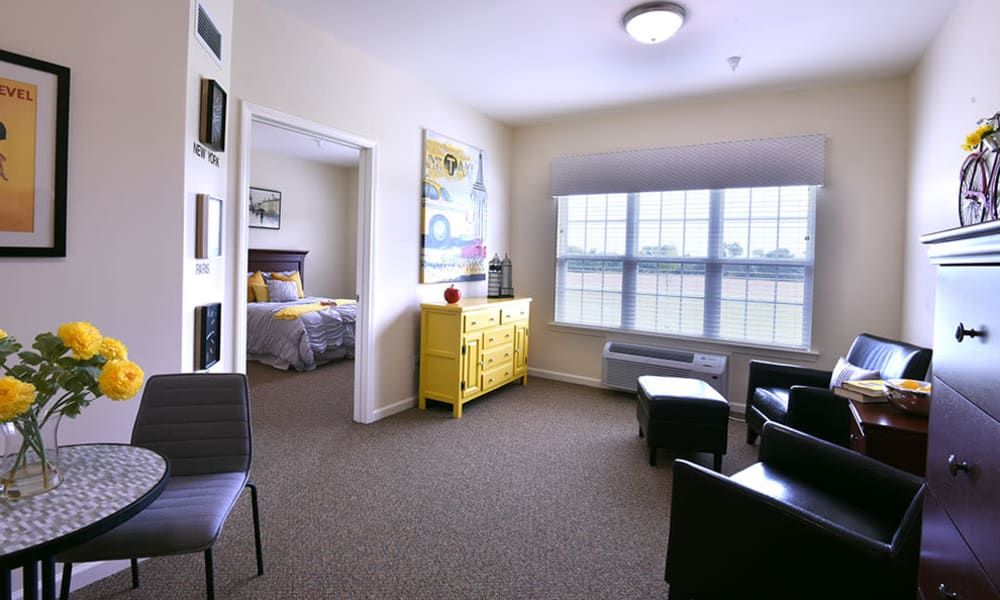 A modern apartment living room with a bright yellow accent piece and natural light streaming in through large windows.