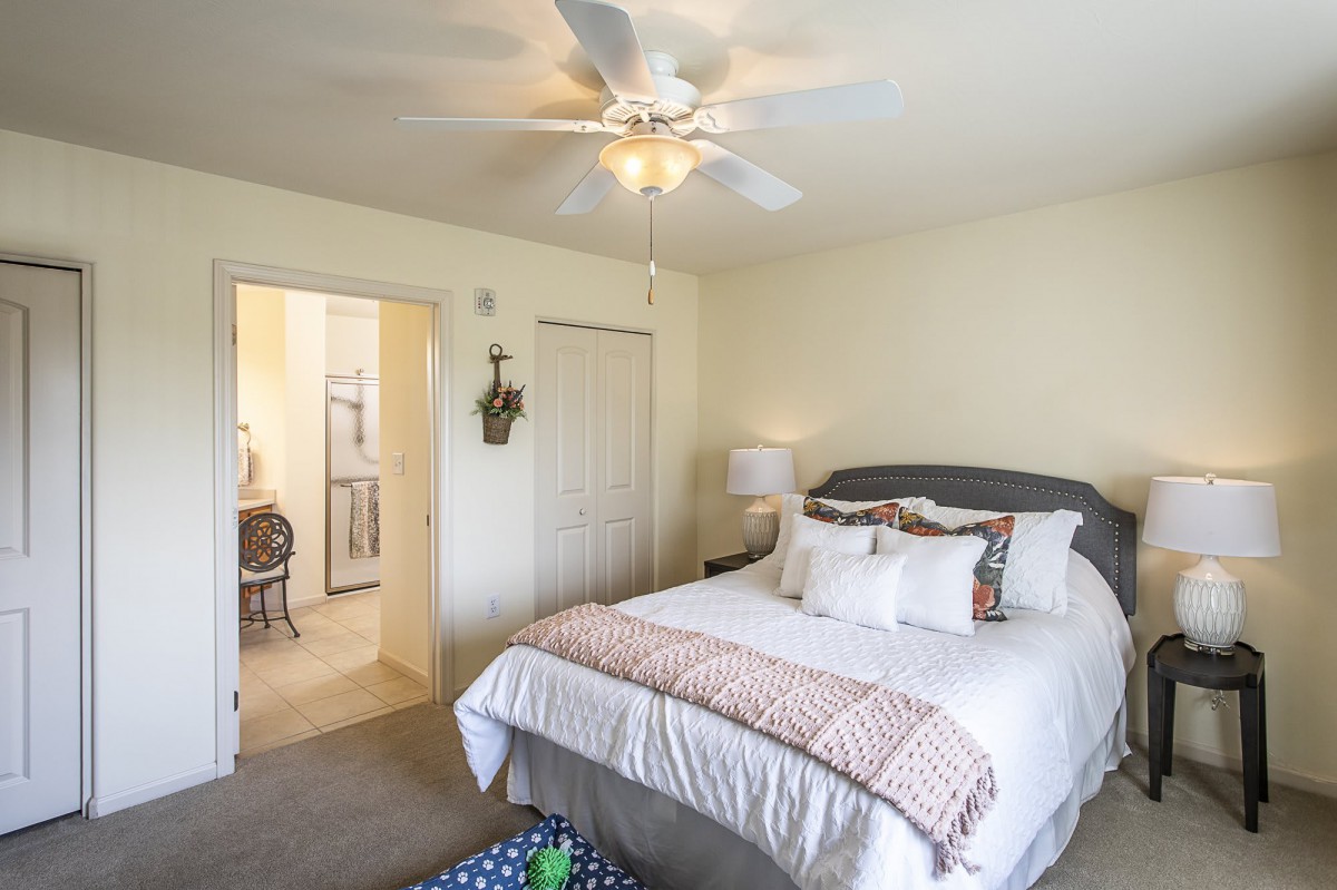 A cozy bedroom with a neatly made bed, ceiling fan, and a lamp beside the bed.