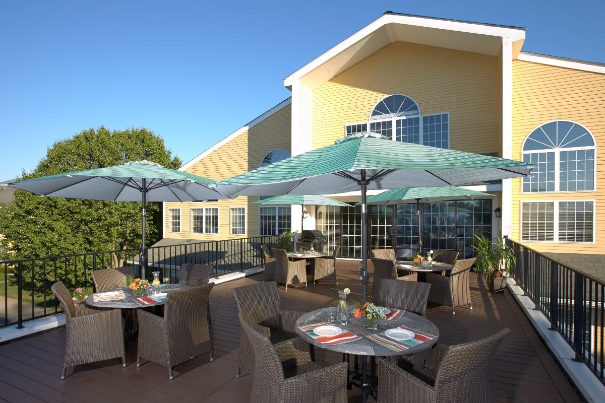 An outdoor dining area with tables, chairs, and umbrellas on a patio beside a building.