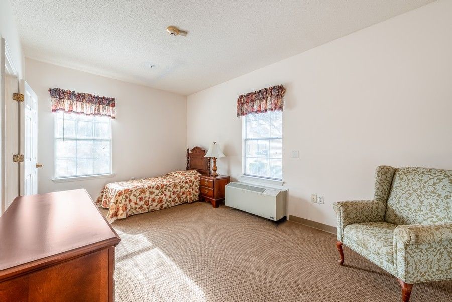 A cozy bedroom with a single bed, two windows, a chair, and a dresser.