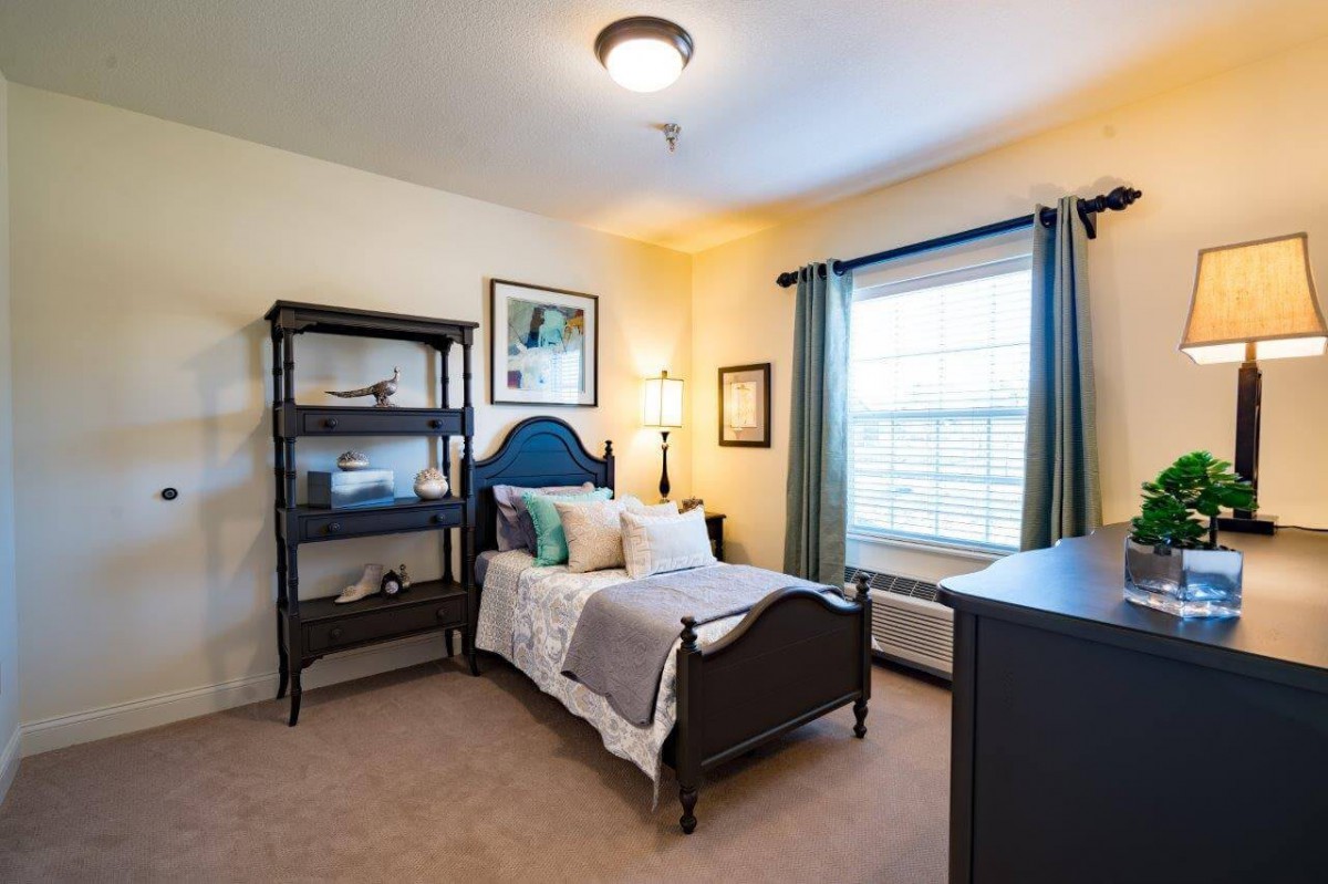 A cozy bedroom with a single bed, shelf, and large window.
