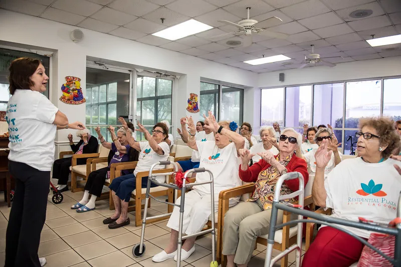 A group of elderly individuals participates in an indoor community activity, sitting on chairs.