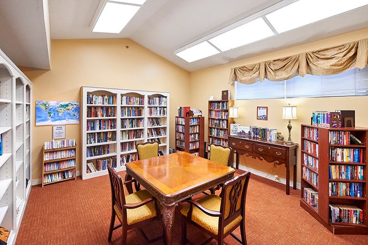 A cozy library room with bookshelves, a table, and chairs under bright lighting.